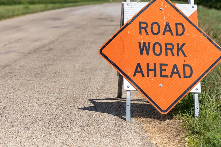 An unpaved, dirt road with a sign that says road work ahead