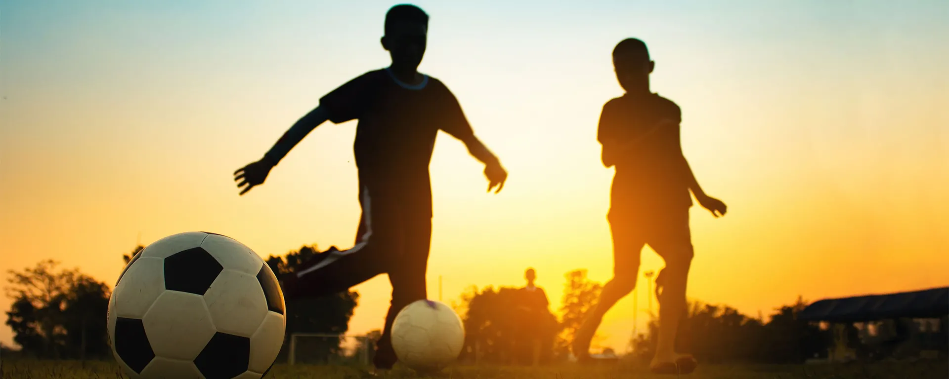 Two children playing soccer during a sunset