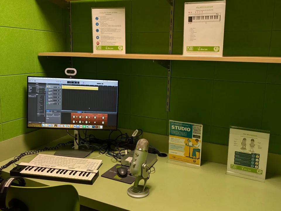 The image shows a small studio with green walls, equipped with a computer, MIDI keyboard, Yeti microphone, and headphones on a desk.