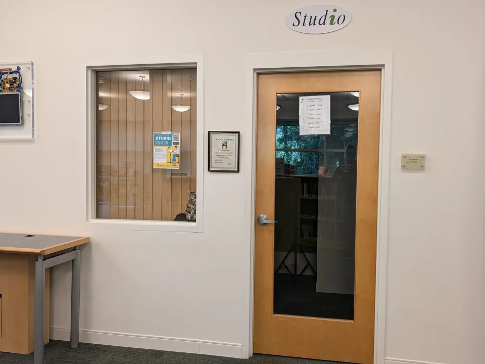 The image shows a library interior with a door labeled "Studio" above it, featuring a wooden frame and a large window,